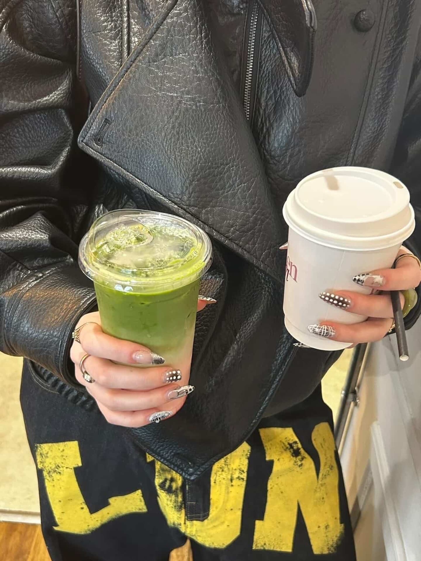 A customer in a leather jacket holding an iced matcha in one hand and a Hidden Gem coffee cup in the other