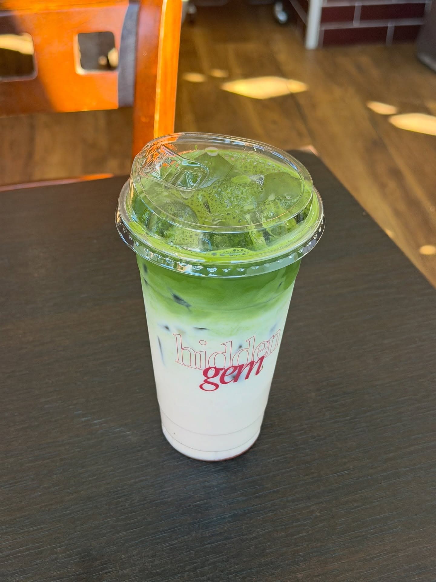 An iced ceremonial matcha in a branded Hidden Gem cup on a café table